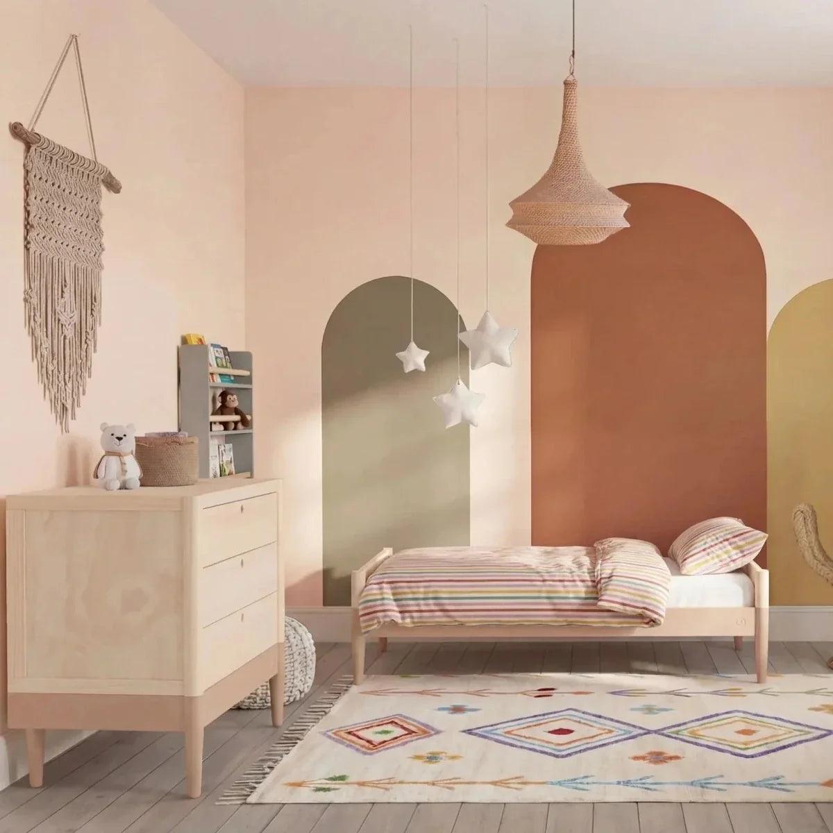 Baby dresser in powder blush and natural ash beside crib in nursery setting