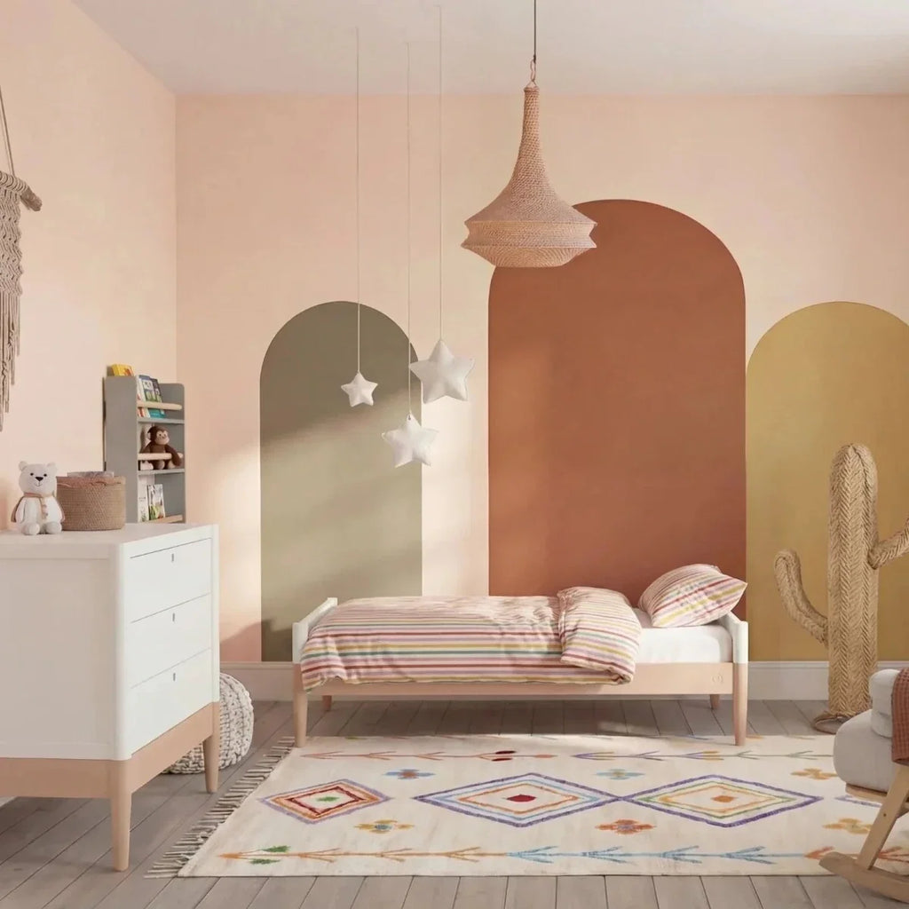 White baby dresser with drawers and powder blush base, partially visible beside crib