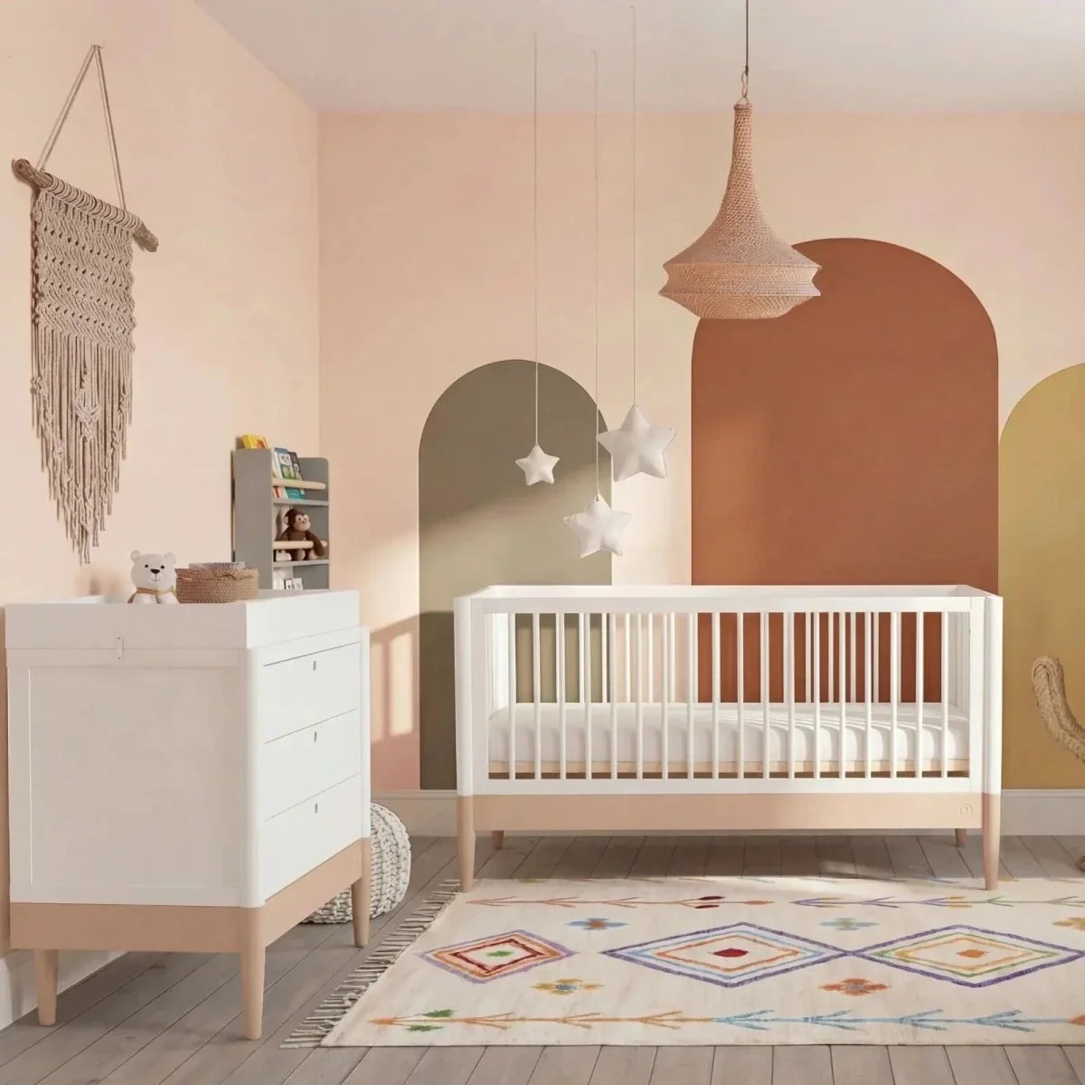 White baby dresser with three drawers, gold knobs, powder blush base, next to crib