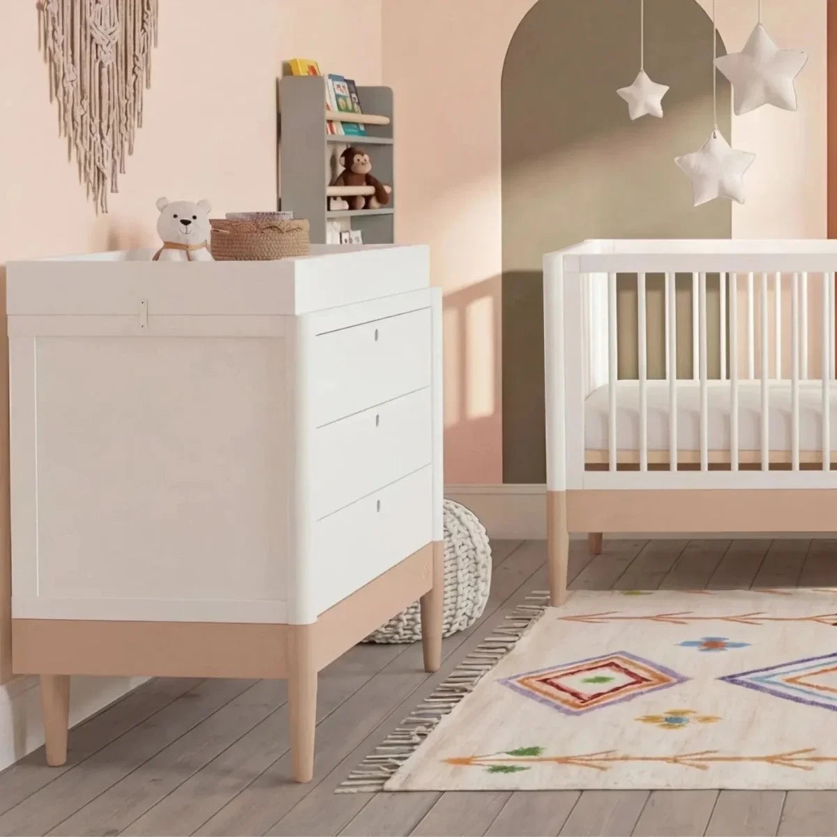 White baby dresser with drawers and powder blush base, beside white crib in nursery