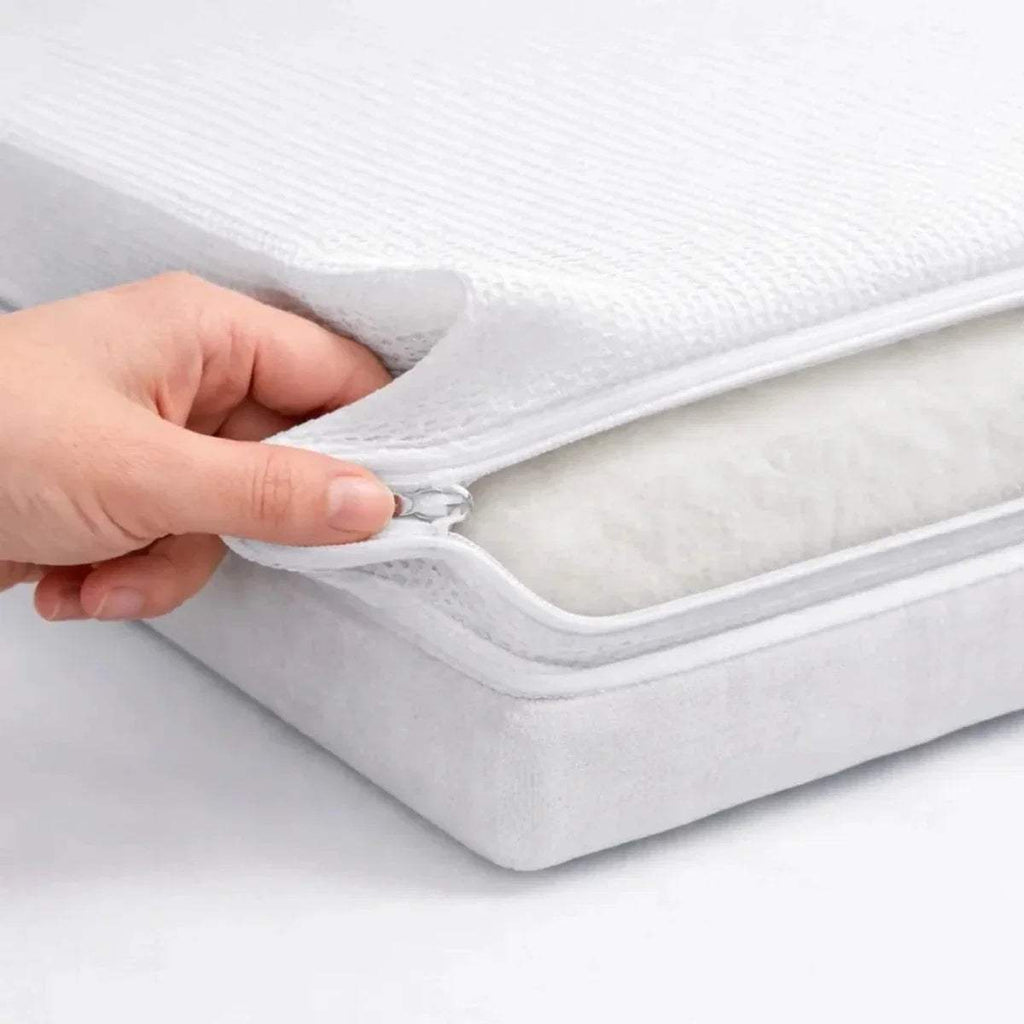 Hand lifting white cover seam on baby cot mattress, showing inner padding layers