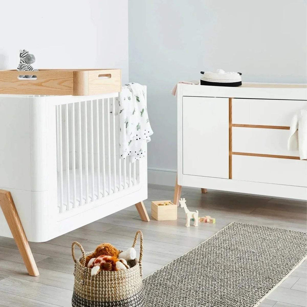 White wooden baby cot bed with natural legs and fitted patterned cover
