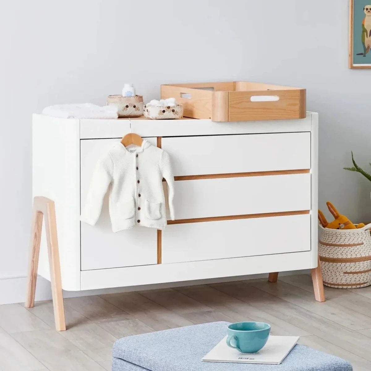 White changing cabinet with natural wood legs and baby jacket on the front