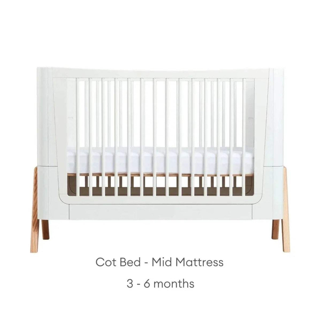 White cot bed frame with vertical slats and natural wood legs, mid platform height