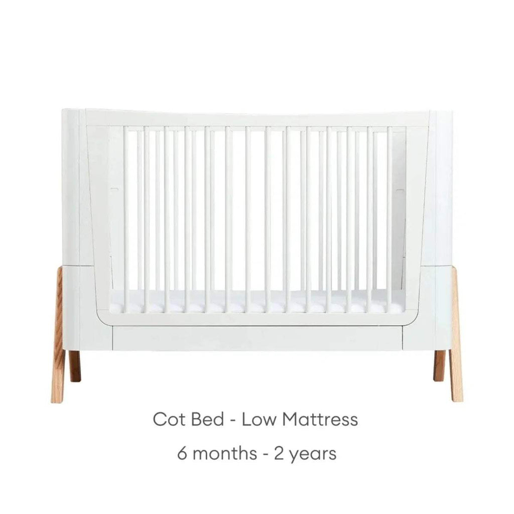 White cot bed frame with vertical slats and natural wood legs, low platform height