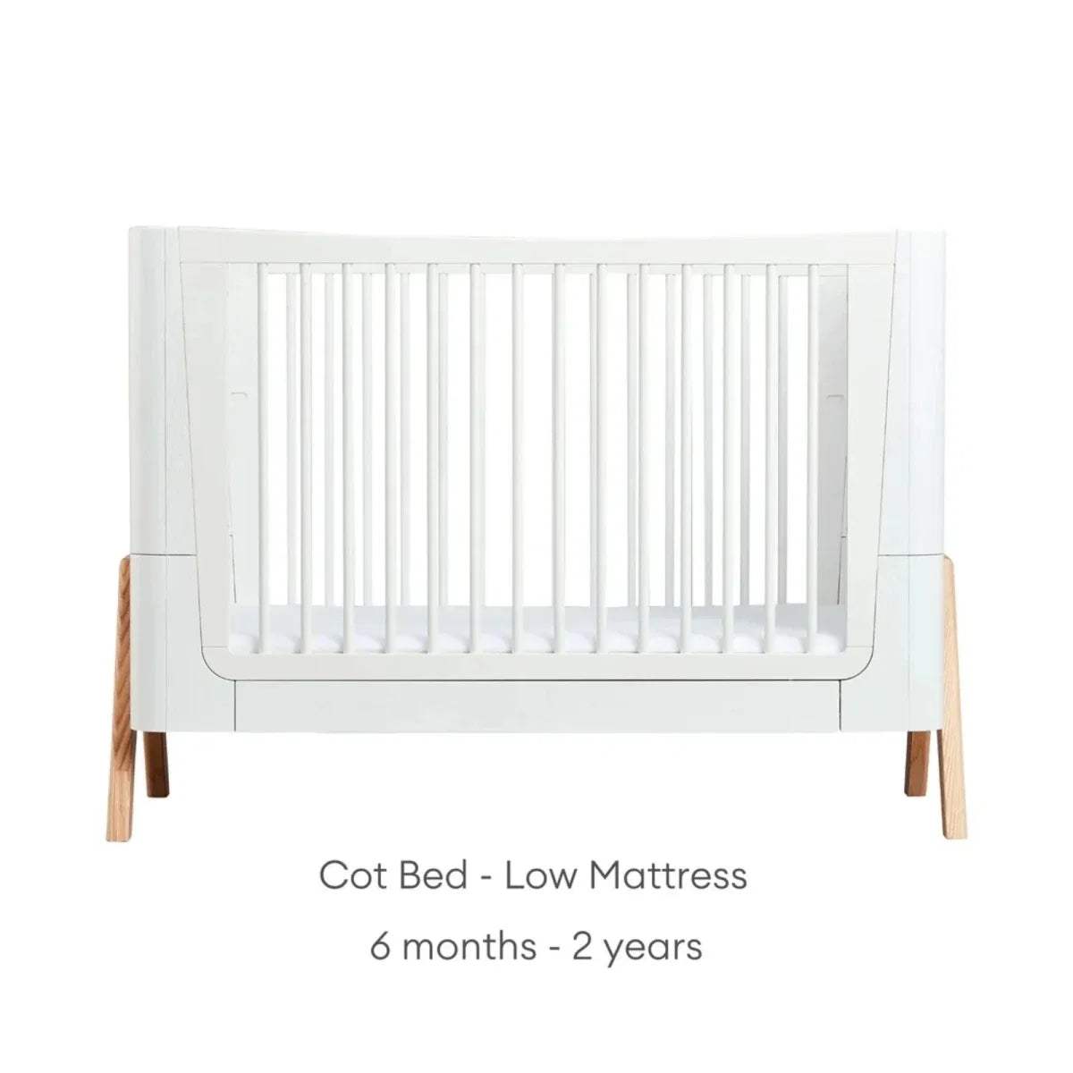 White cot bed frame with vertical slats and natural wood legs, low platform height