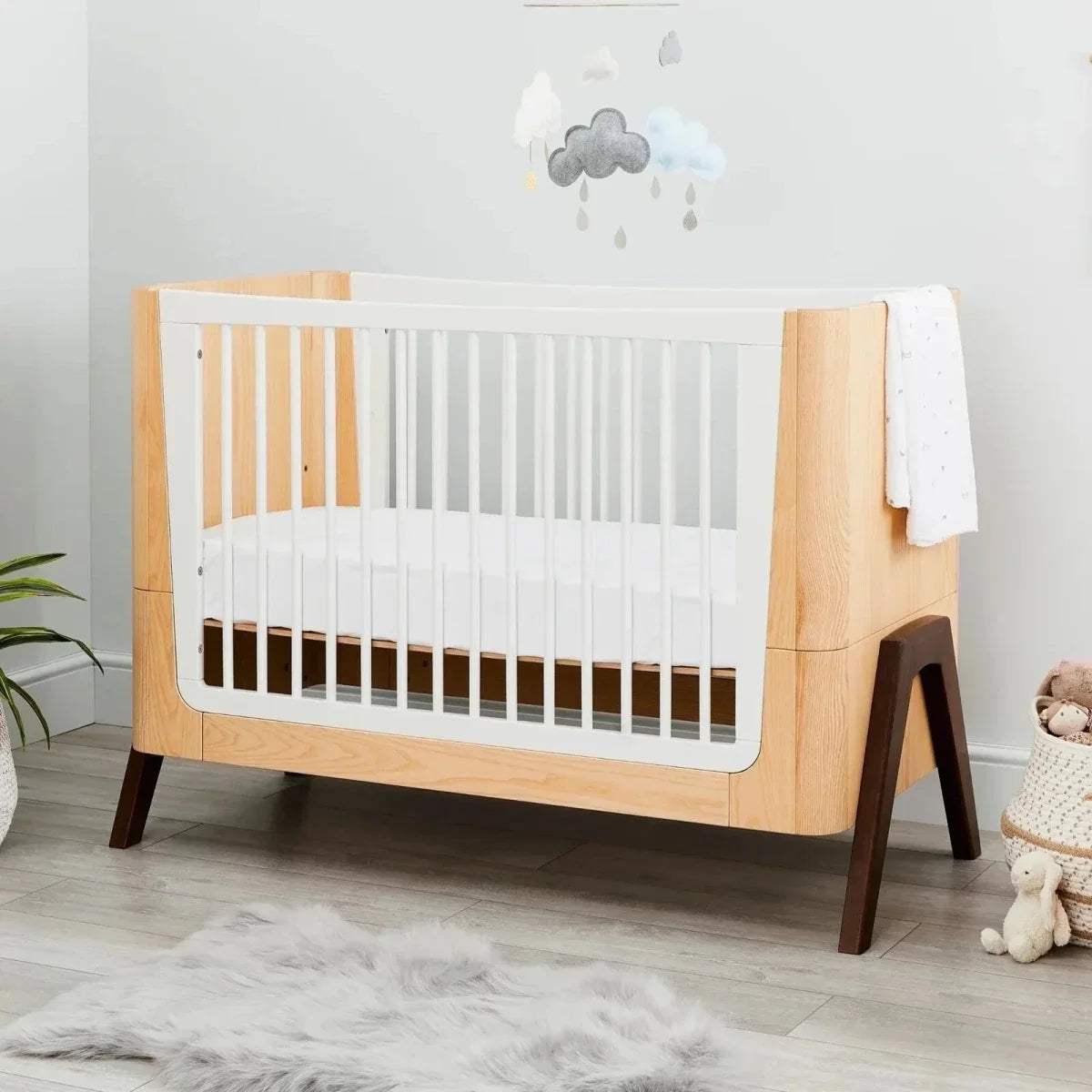 Natural wood baby crib with white slat panels and dark walnut-style legs