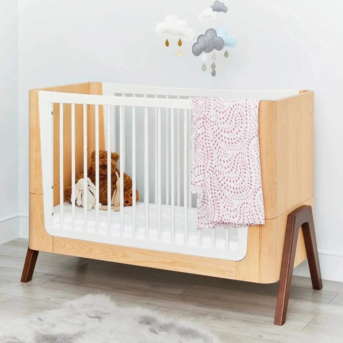 Natural wood baby crib with white slats and pink crochet blanket draped over rail