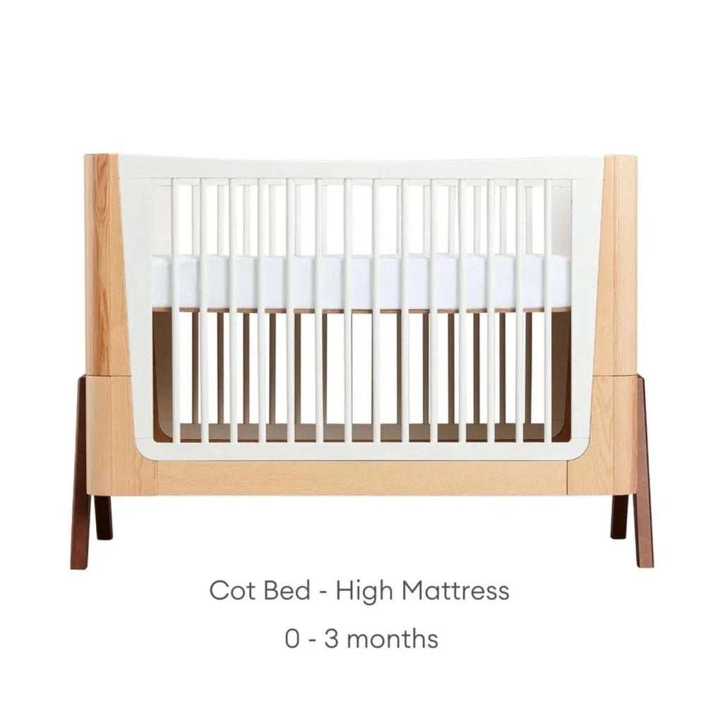 Natural wood baby cot bed with white slatted sides and high mattress position