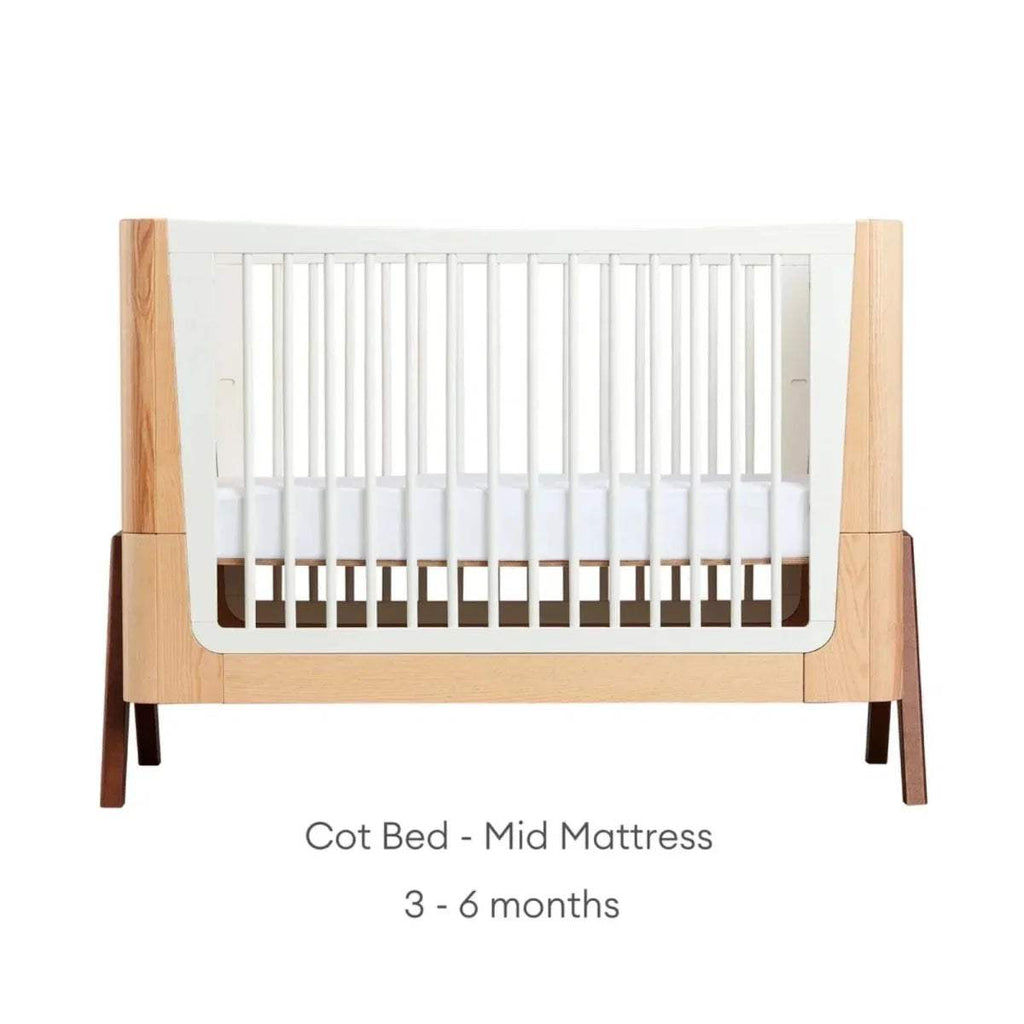 Natural wood baby cot bed with white slatted sides and mid mattress position