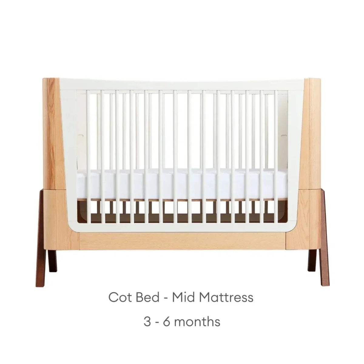 Natural wood baby cot bed with white slatted sides and mid mattress position