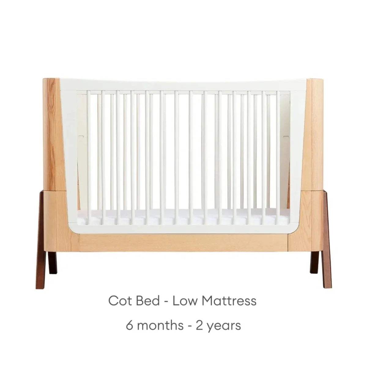 Natural wood baby cot bed with white slatted sides and low mattress position