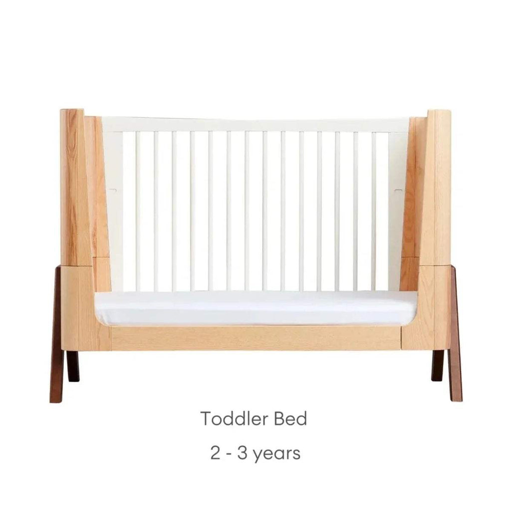 Natural wood toddler bed with white slatted side rails and front guard