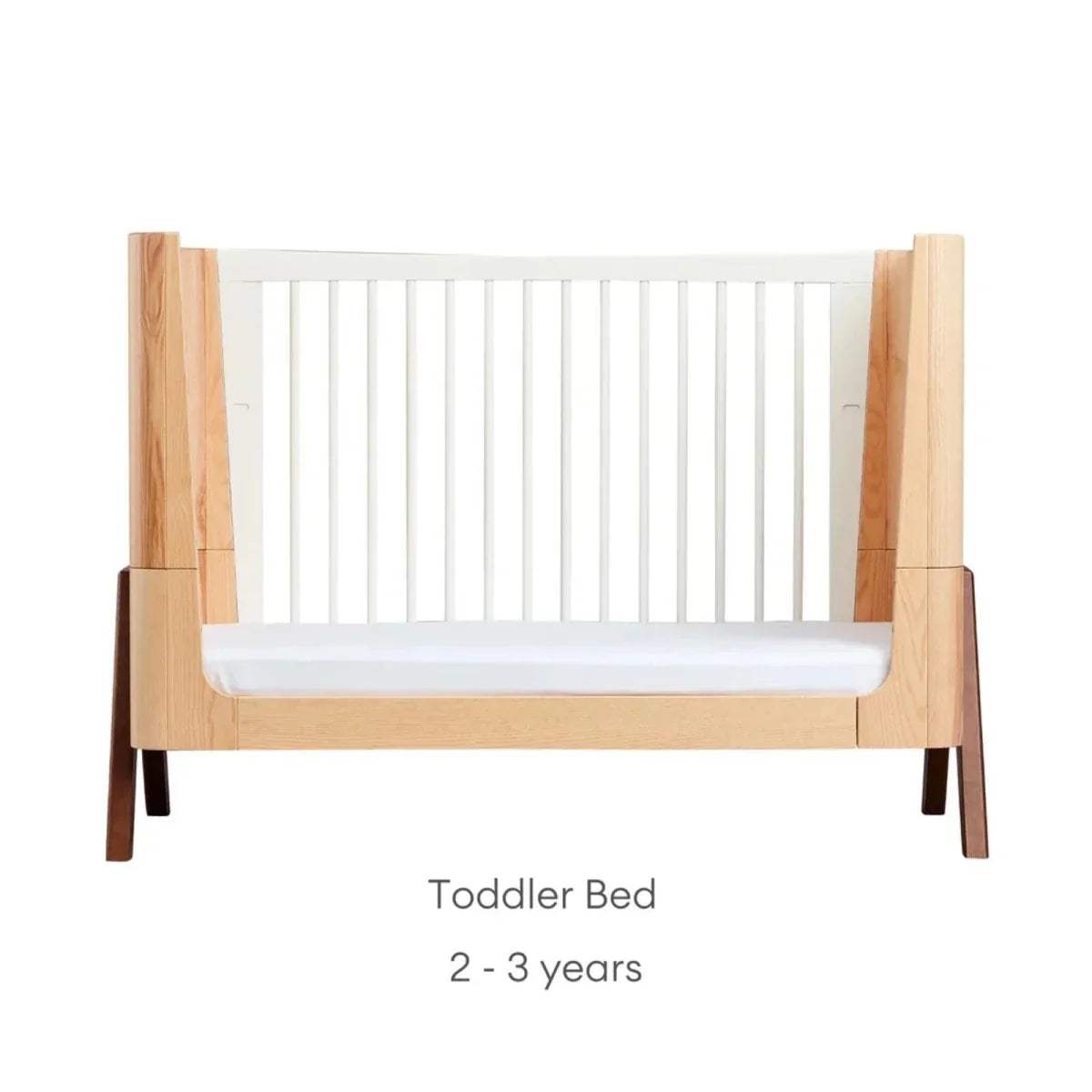 Natural wood toddler bed with white slatted side rails and front guard