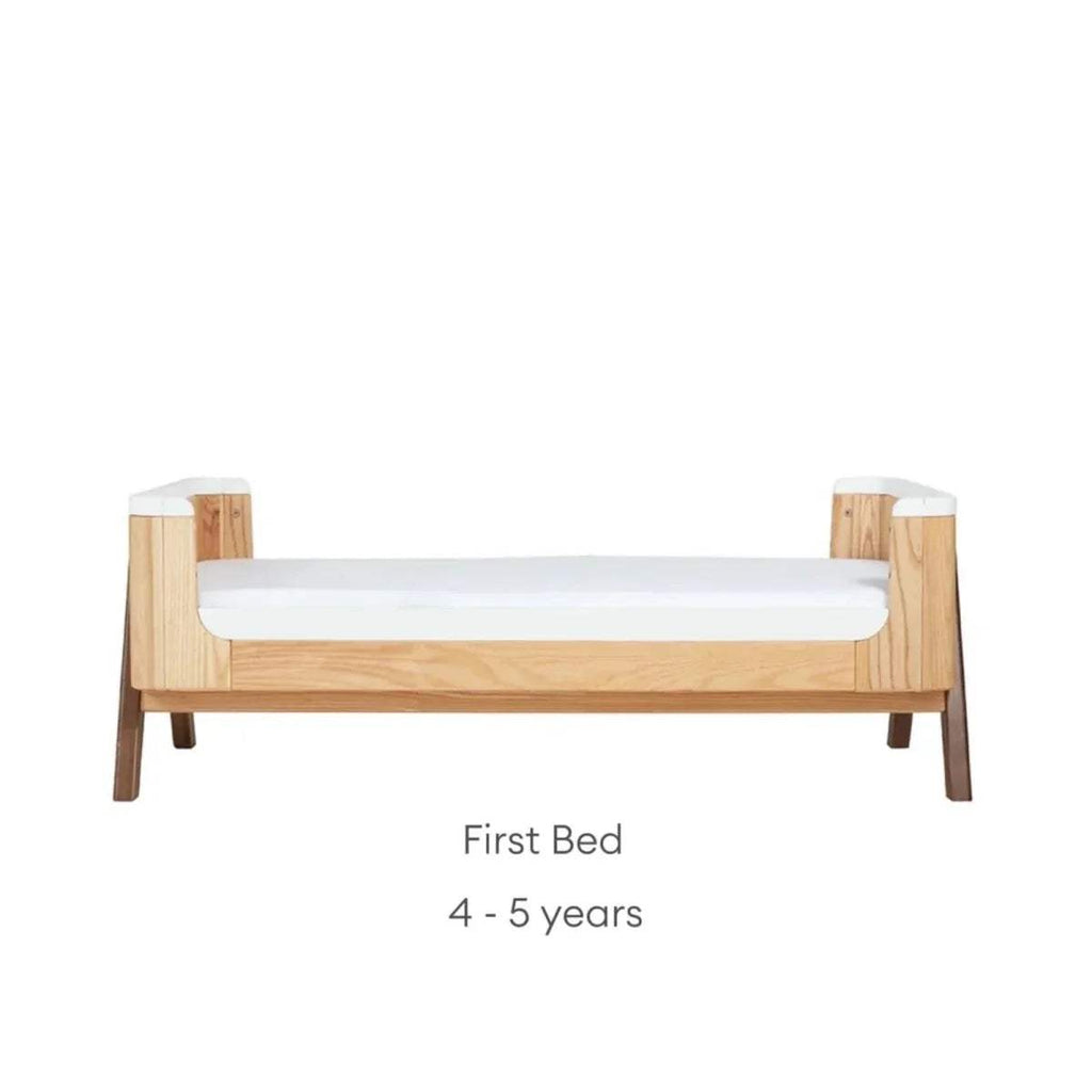 Natural wood first bed with white slatted side rails and sturdy legs