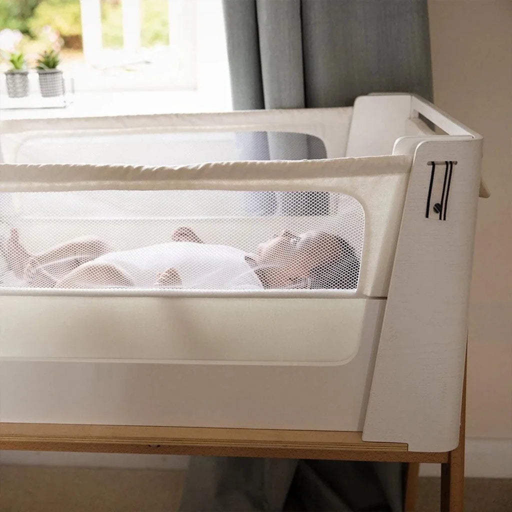 White bedside crib end with mesh panel and natural wood base