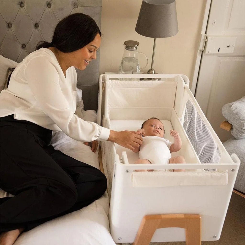 White bedside crib with open top rail and mesh side for baby access