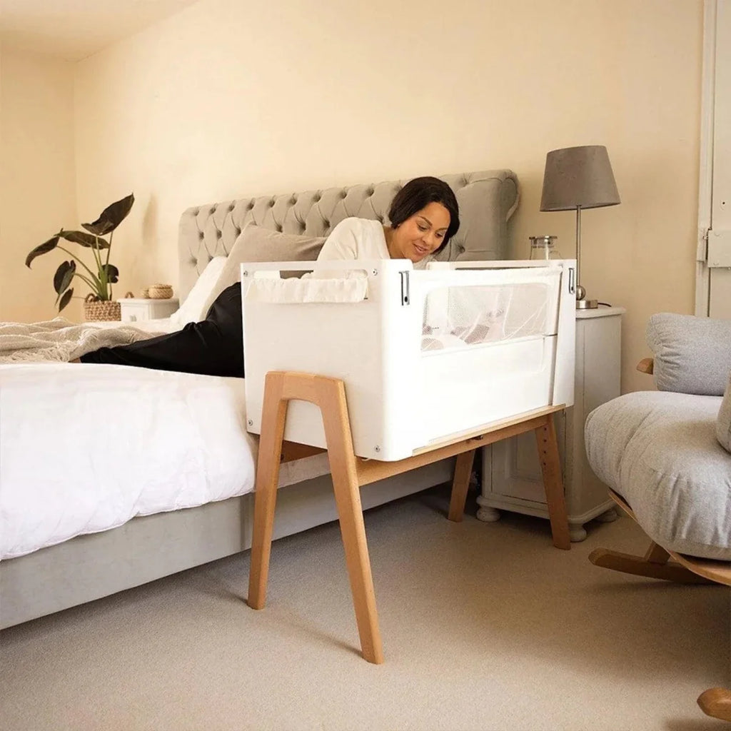 White and natural bedside crib with mesh barrier and solid wood legs