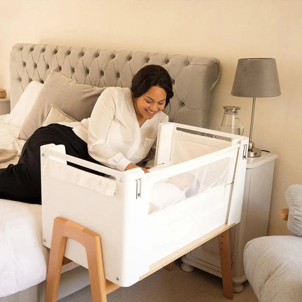 White bedside crib with mesh opening and natural wood support rails