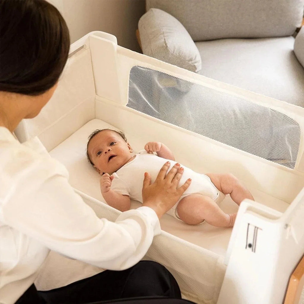 White and natural baby bedside crib with mesh side panel and padded interior
