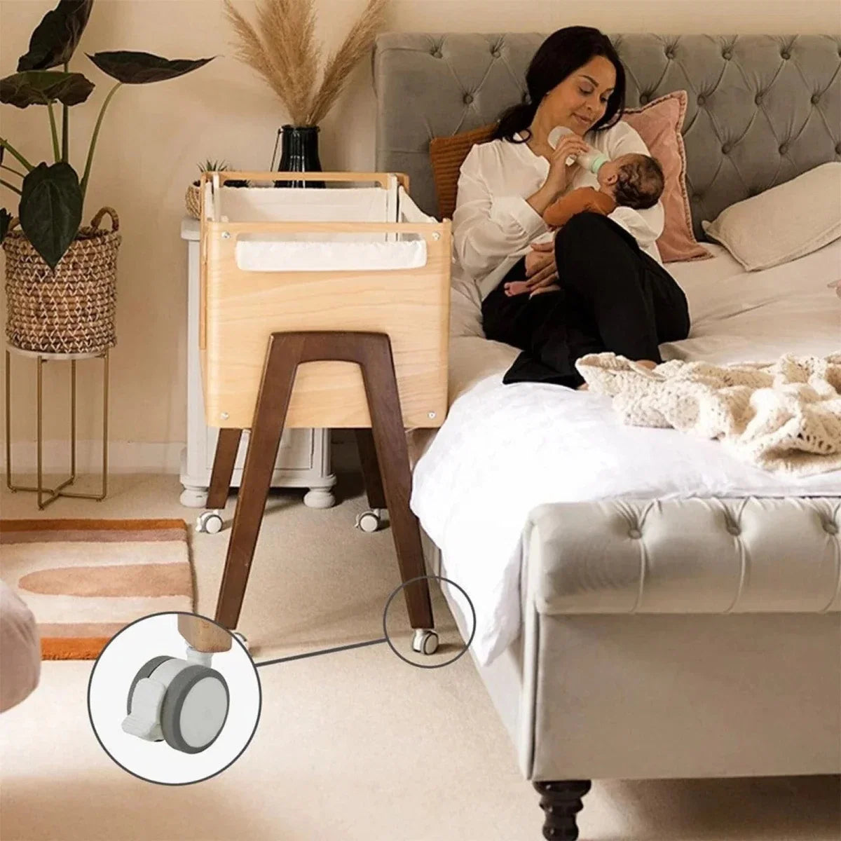 Baby bedside crib next to bed with white frame, natural wood legs, and wheels