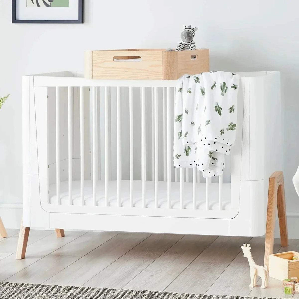 Natural wood changing station with a white crib-style base and top platform