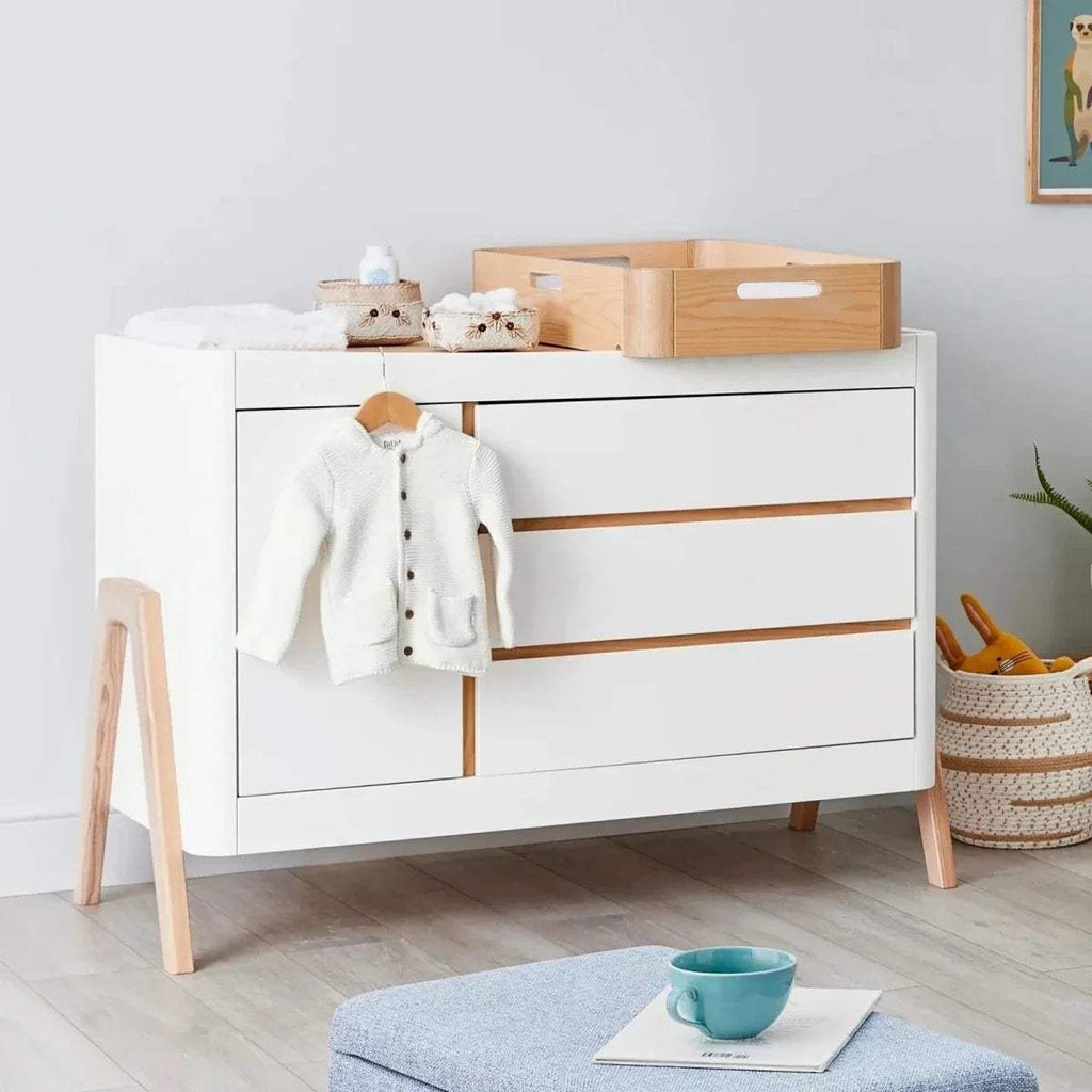 Baby dresser in white with natural wood top, two doors, and drawer accents.
