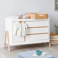 Baby dresser in white with natural wood top, two doors, and drawer accents.