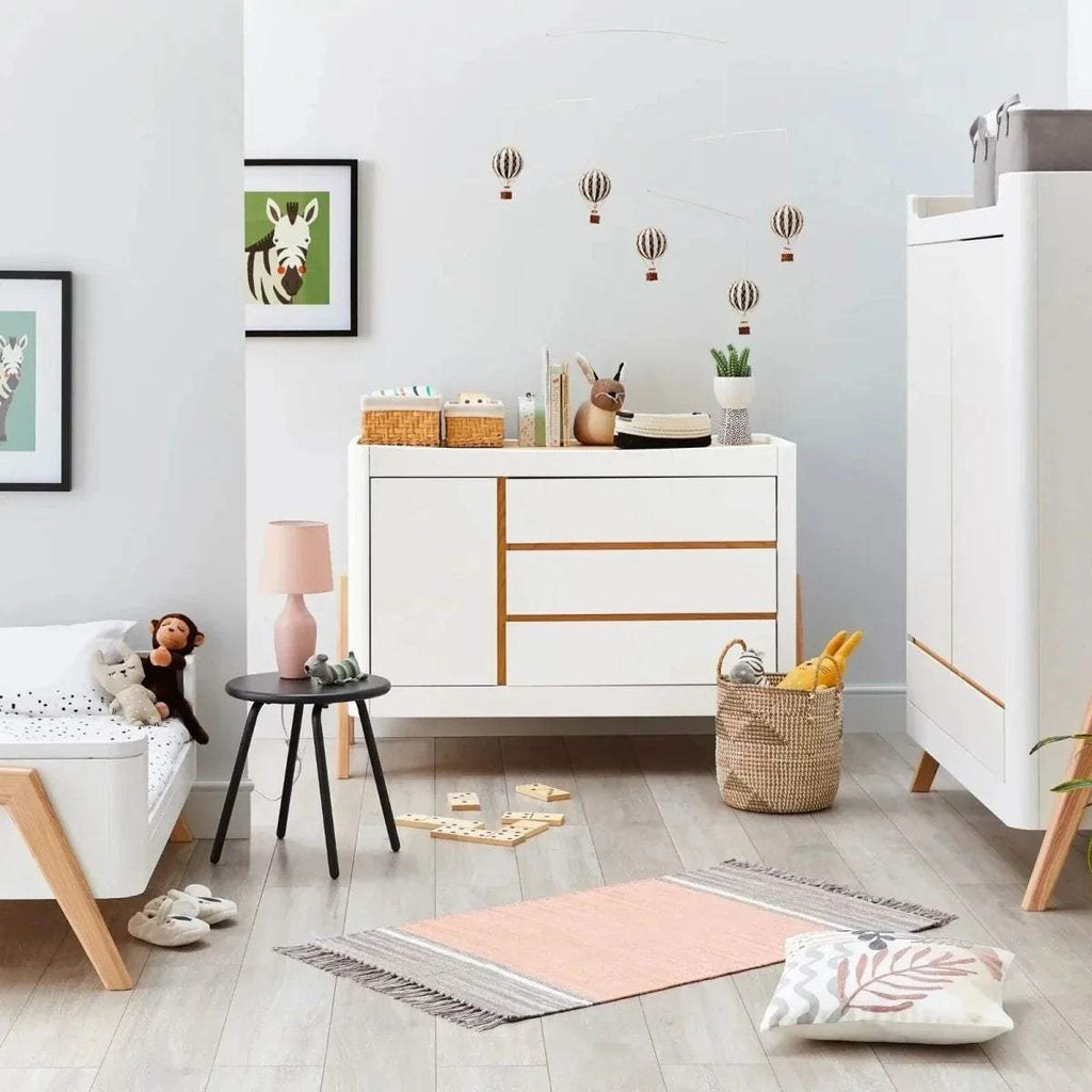 White baby dresser with natural wood legs and horizontal trim across the front.