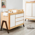 Natural wood baby dresser with white drawers and dark-stained tapered legs
