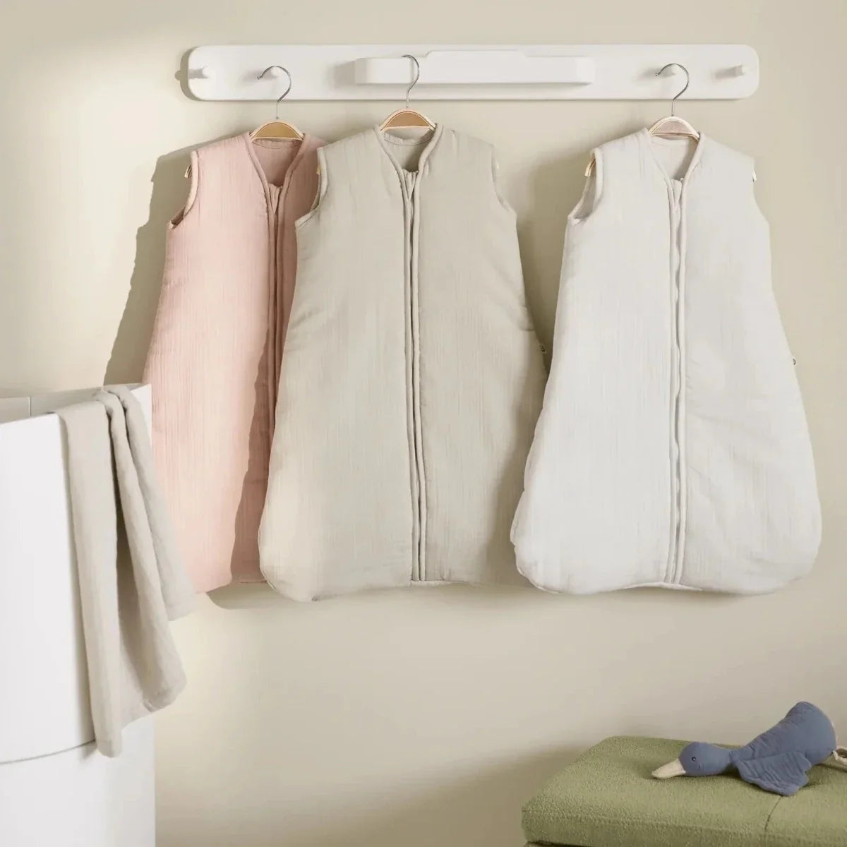 White hanging rail with three hangers displaying sleeveless baby sleeping bags