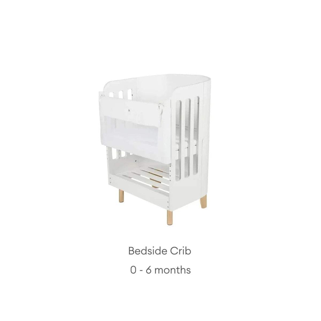 White bedside crib with vertical slat guard and natural wooden legs