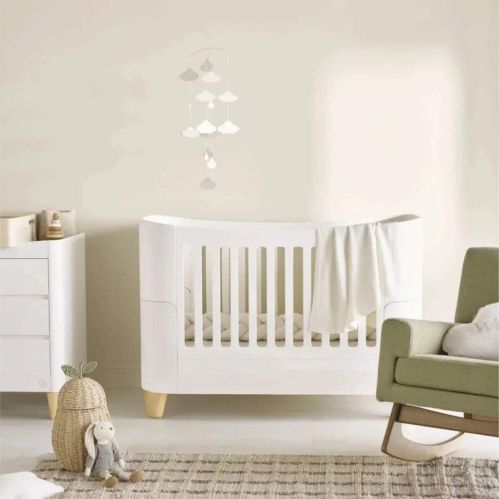 White cot bed with vertical slat guard and natural wooden legs