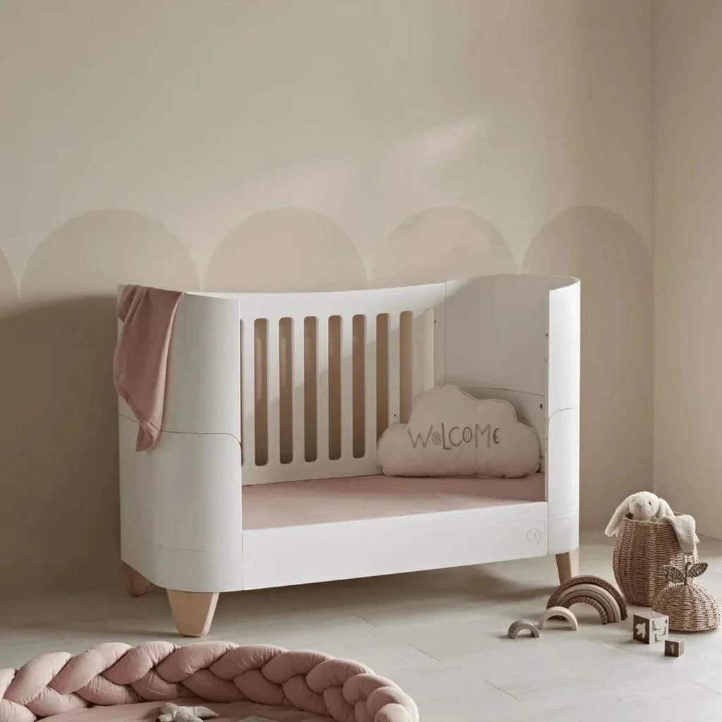 White cot bed with slatted sides, padded mattress and natural-pink bedding set