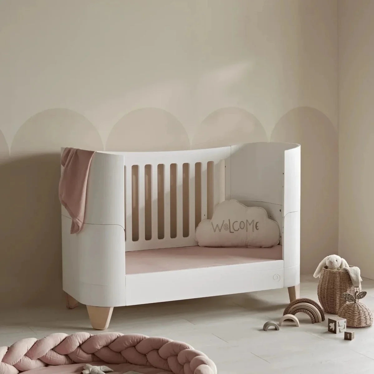 White crib-style bed with low front rail and central slatted panel, natural wood legs
