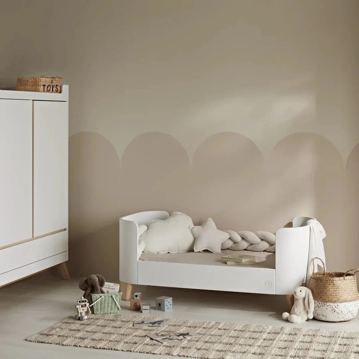 White cot bed with curved end panels and slatted side rails, natural wood feet