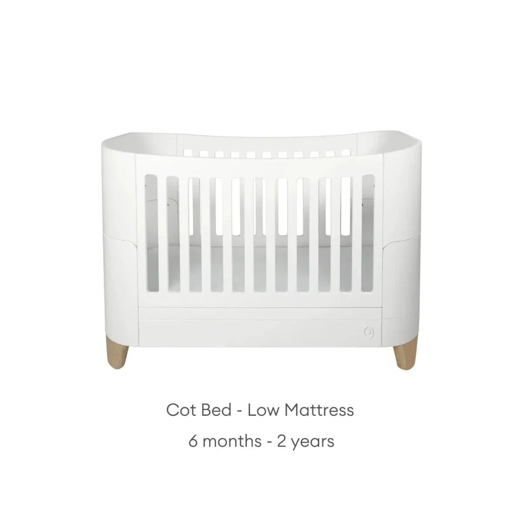 White cot bed frame with low mattress position, vertical slat front, and natural legs