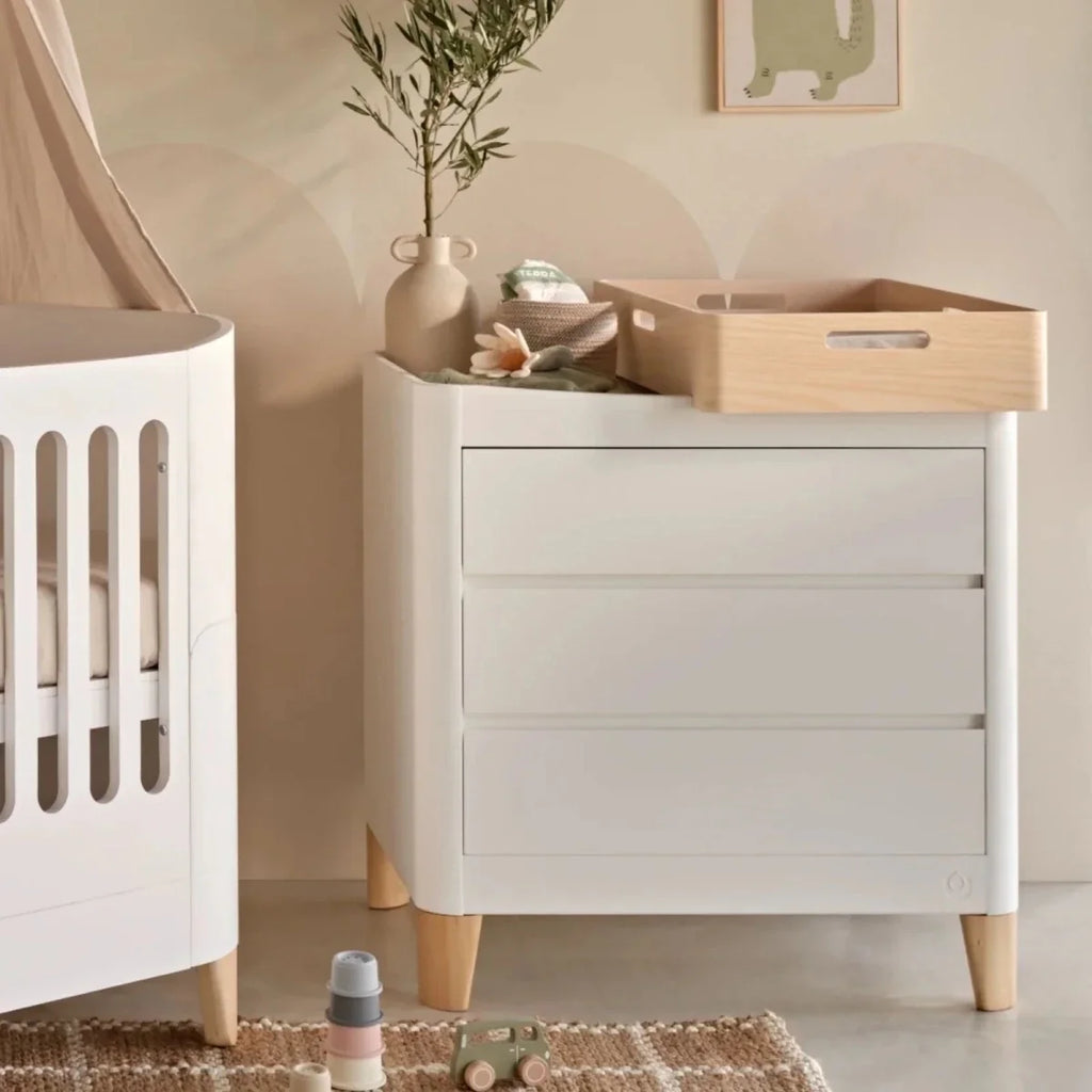 White baby dresser with wide front cabinet door, drawers, and natural wood feet
