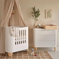White mini cot with vertical slat sides and fitted mattress, styled in a nursery