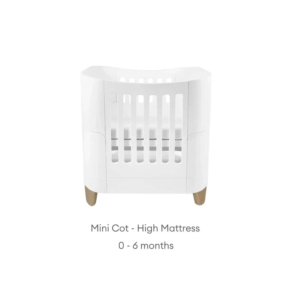 White mini cot bed with curved sides and vertical slats; high mattress.