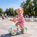 Green toddler balance bike with orange seat and glowing LED wheels, toddler riding outdoors