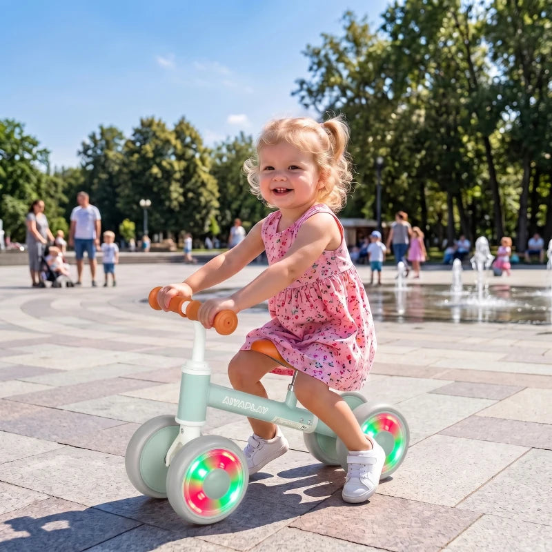 Green toddler balance bike with orange seat and glowing LED wheels, toddler riding outdoors
