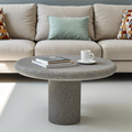 Round stone coffee table in front of a beige sofa with decorative pillows.