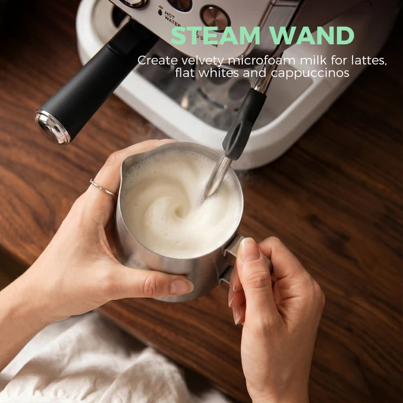 Black steam wand frothing milk in a metal cup beside a white machine