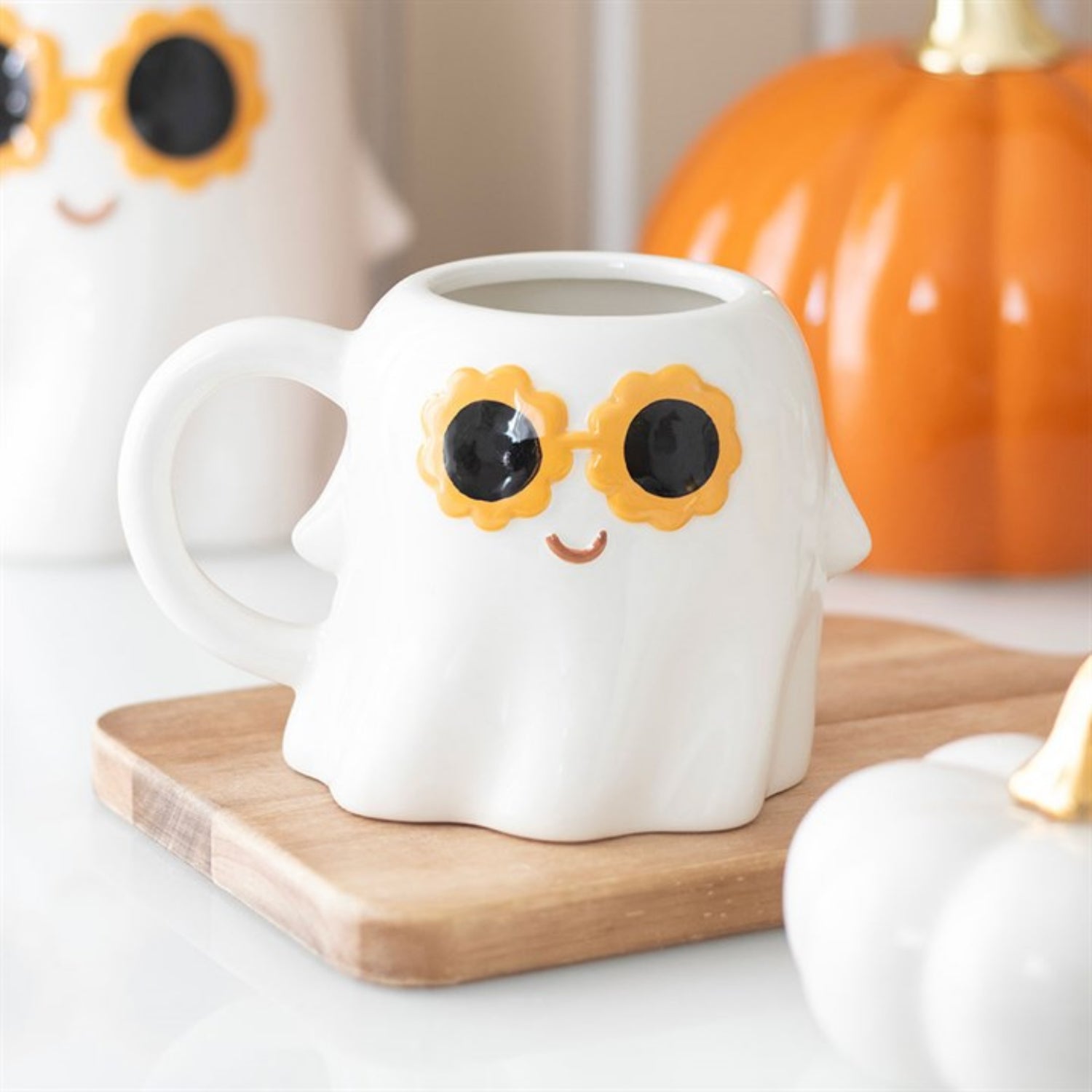 White mug with sunflower design on a wooden coaster with pumpkins in the background