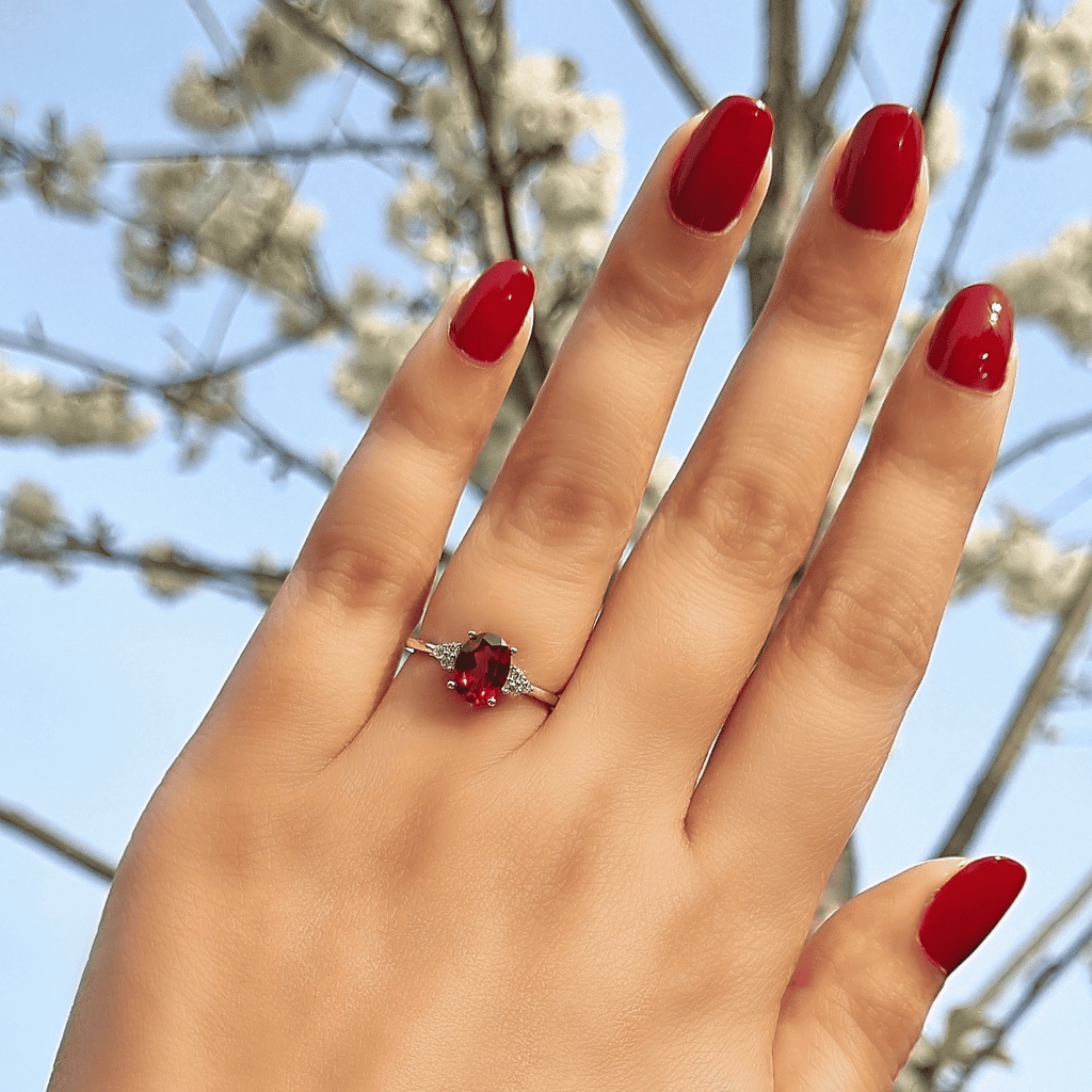 Sterling silver garnet ring on finger with oval red center gemstone and side sparkle