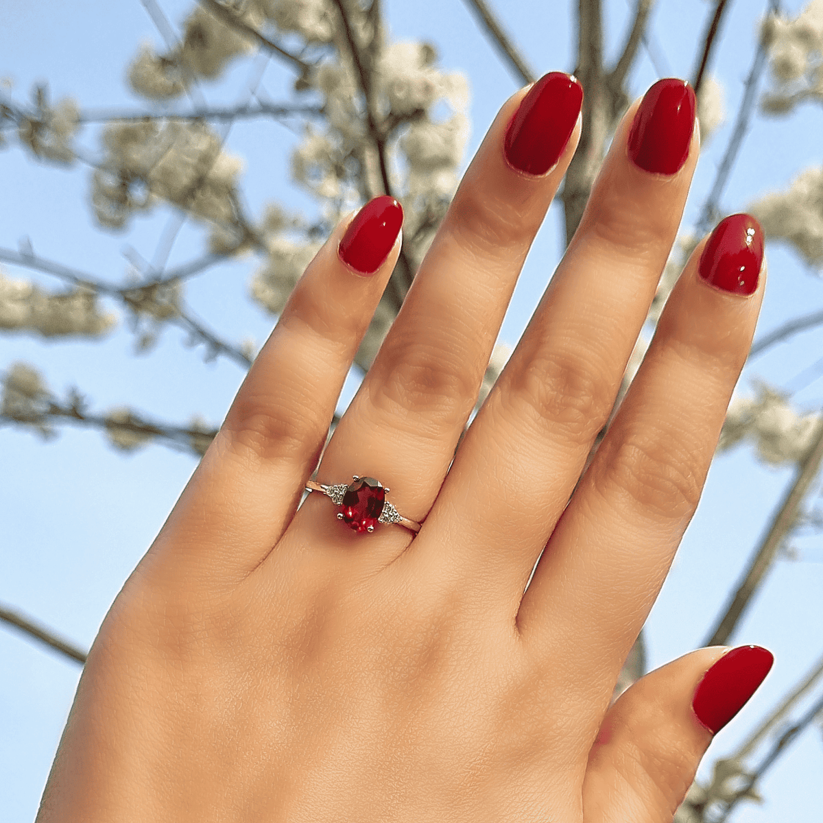Sterling silver garnet ring on finger with oval red center gemstone and side sparkle
