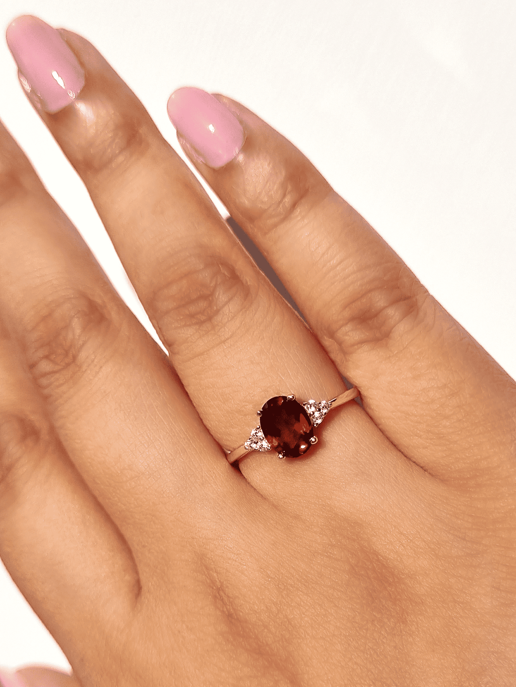 Gold vermeil ring on hand with oval red garnet center and two clear stones