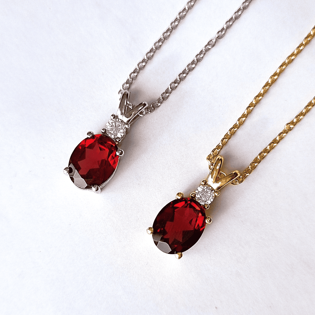 Two garnet pendant necklaces with oval red stones and diamond accents on silver and gold chains