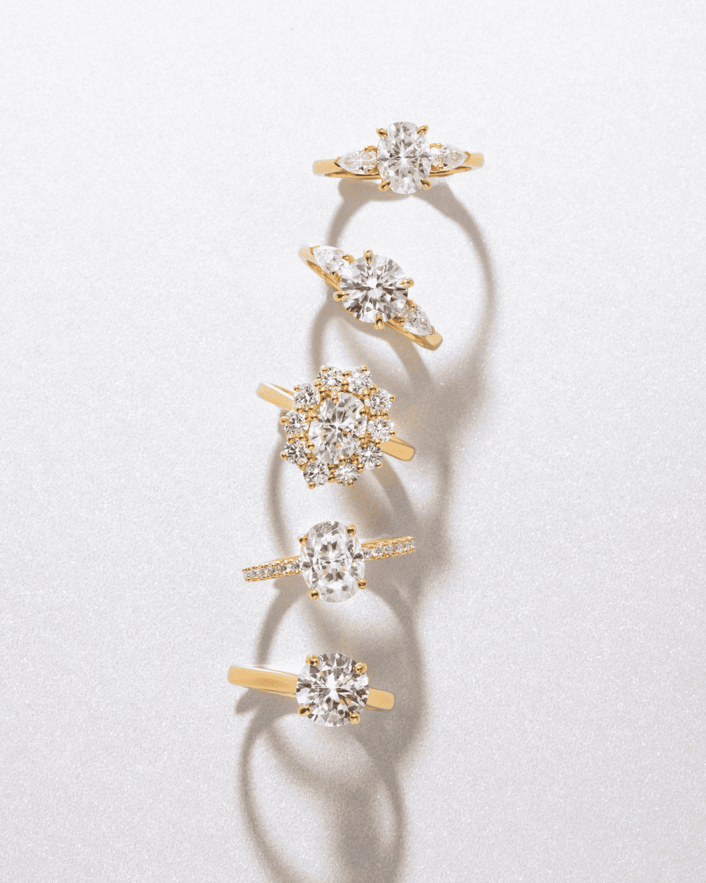 Multiple oval moissanite three-stone rings with gold-tone bands arranged vertically